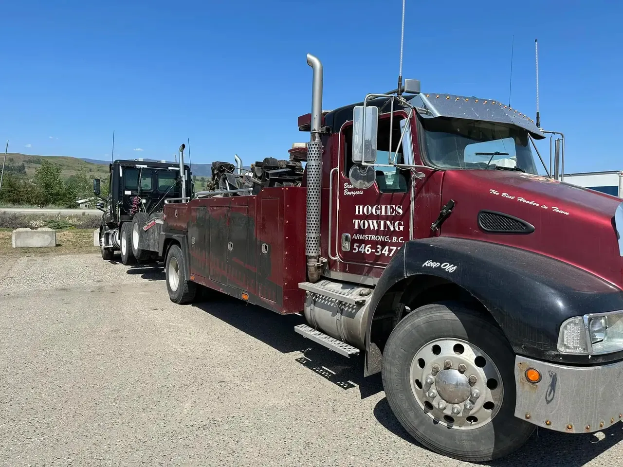 Hogie's maroon Kenworth heavy wrecker towing a semi truck on a sunny day