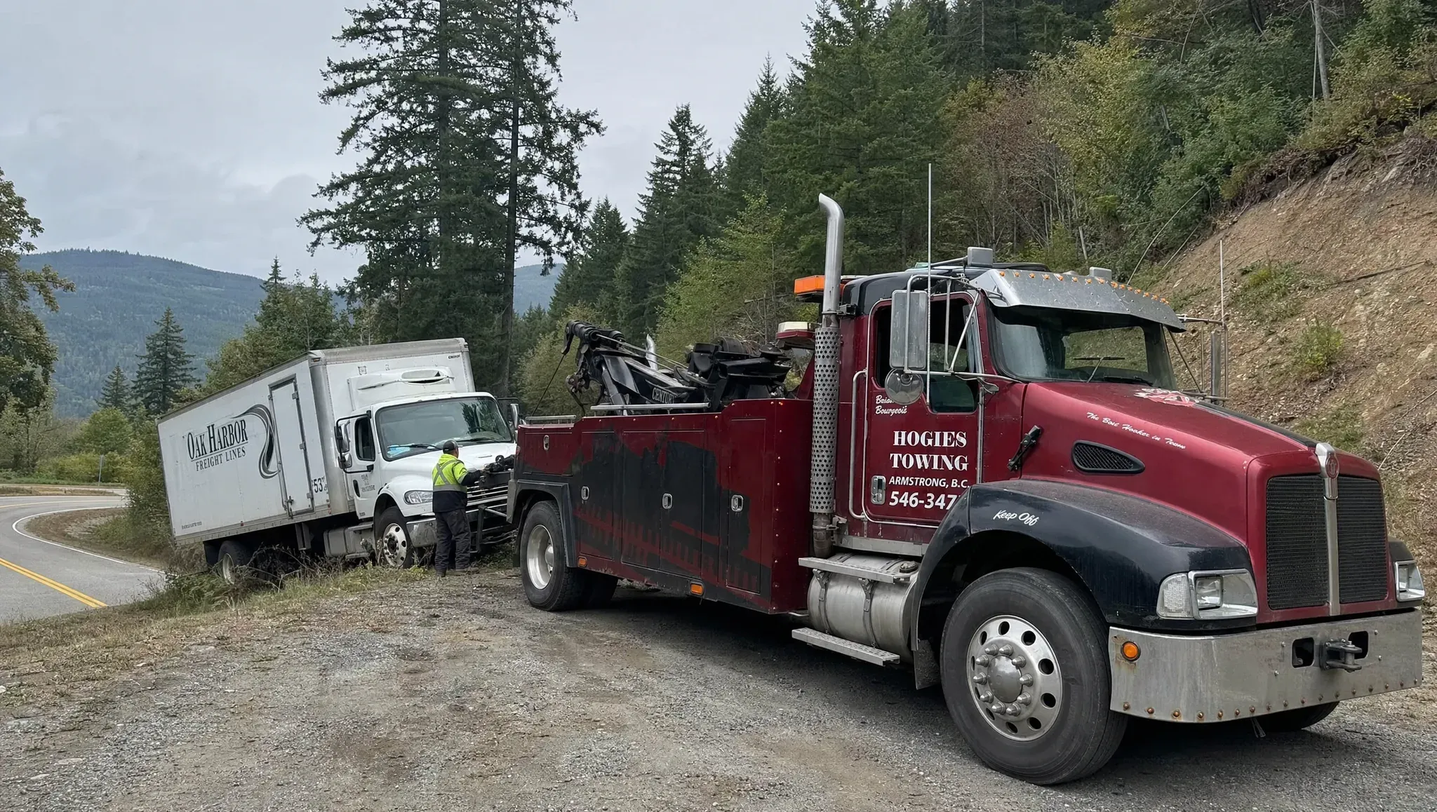 Hogie's heavy wrecker winching a box truck back onto a forested BC highway