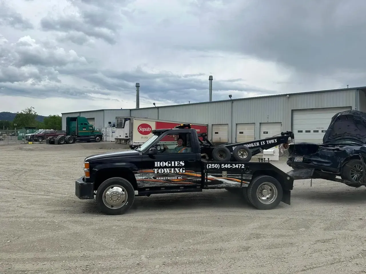 Hogie's black Chevy wrecker with a pickup truck hooked on the lift, leaving the yard